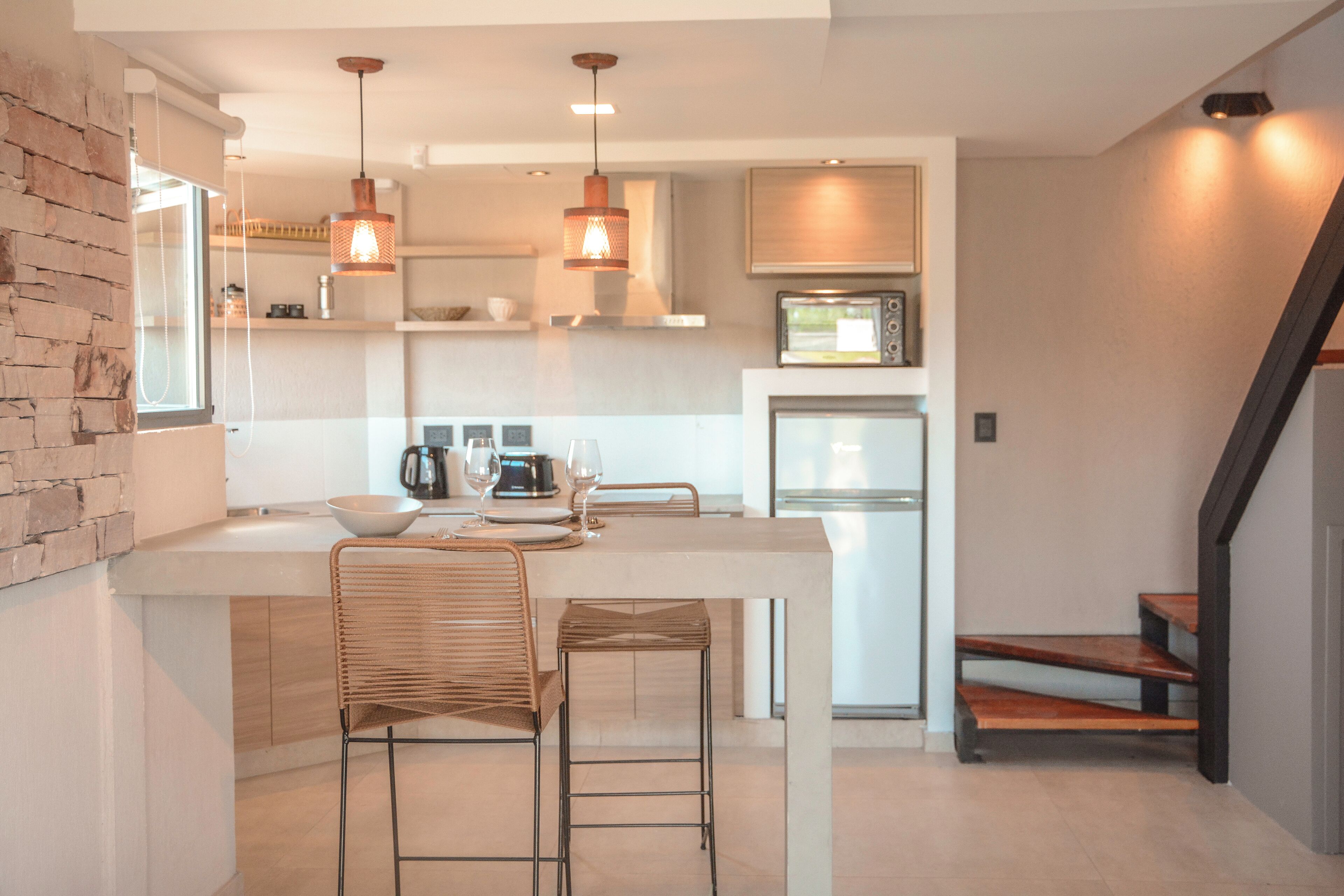Una cocina moderna con una isla central, dos taburetes de bar, iluminación colgante y un microondas.