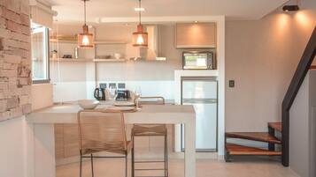 Una cocina moderna con una isla central, dos taburetes de bar, iluminación colgante y un microondas.