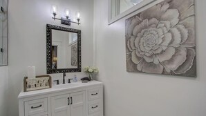 Un bagno con un mobile lavabo bianco, un ampio specchio con cornice decorativa e un'opera d'arte floreale appesa al muro.