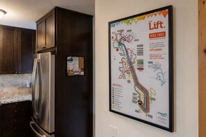 Een keuken met donkere houten kastjes en een roestvrijstalen koelkast. Op de muur hangt een kleurrijke kaart van een openbaar vervoersnetwerk.