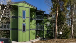 A multi-story building with a green facade, balconies, and a parking area. - Mountain Views from WP Top Floor Getaway (Winter Park)