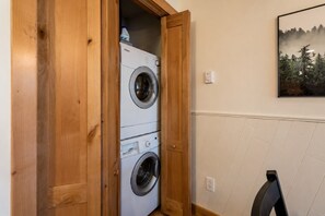 A laundry room with two stacked washing machines, a wooden door, and a wall-mounted outlet.
