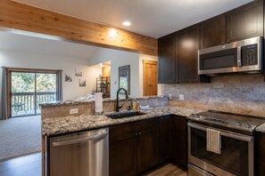 A modern kitchen with granite countertops, stainless steel appliances, and wooden ceiling beams.