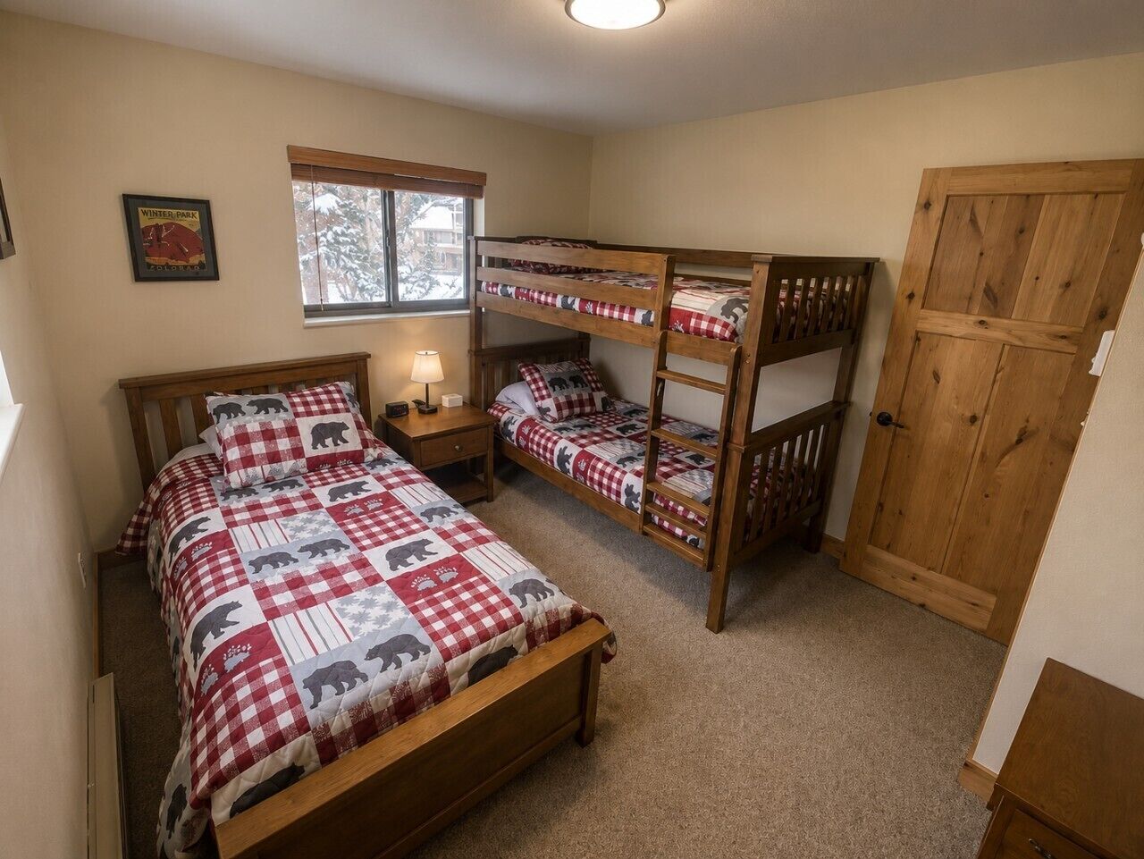 Une chambre avec deux lits superposés, un lit simple, une table de chevet avec une lampe, une fenêtre avec des stores et une porte.