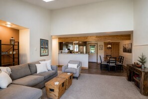 A spacious living area with a sofa, coffee table, and wooden storage boxes. A kitchen and dining area are visible in the background.