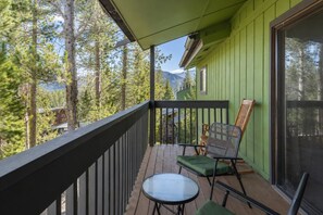 A wooden deck with a green railing, a table, and two chairs.