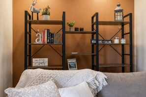 A cozy living room with a sofa, decorative pillows, a bookshelf with books and a sign, and a small plant.