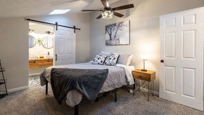 Un dormitorio con cama, mesita de noche, lámpara y ventilador de techo.