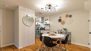 Un área de comedor con una mesa redonda, sillas negras y un espejo en la pared.