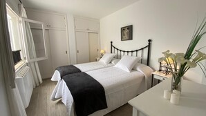 Habitación doble con dos camas, paredes blancas, una lámpara en el techo y un cuadro en la pared.