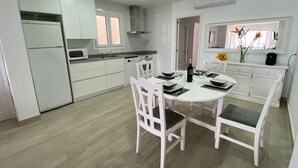 Cocina moderna con armarios blancos, microondas y comedor con mesa redonda y sillas blancas.