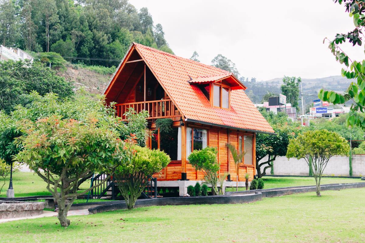 Una casa de fusta amb teulada vermella, envoltada de verdura i un jardí petit.