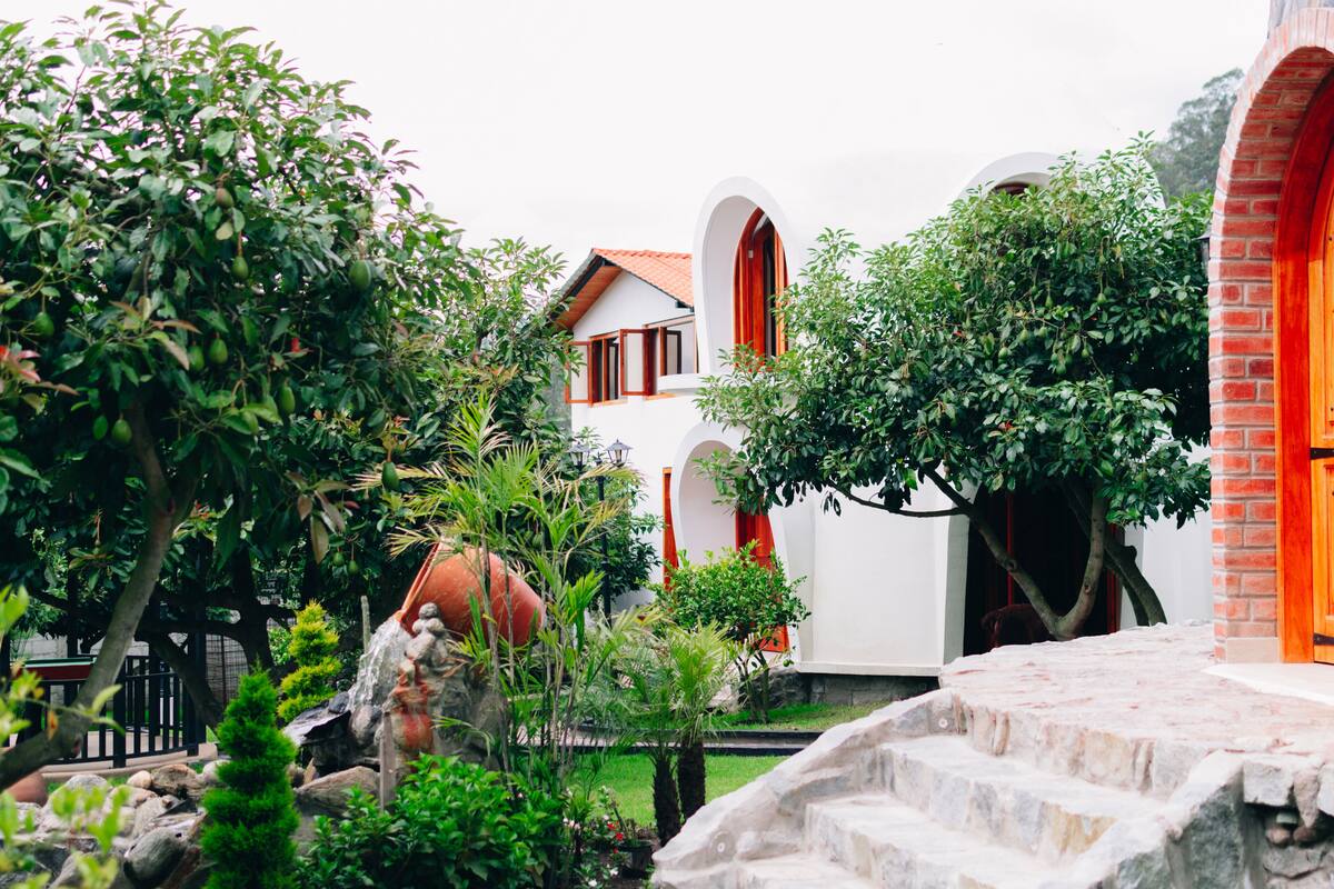 Un pati amb una escala de pedra, un edifici blanc amb accents vermells i vegetació abundant.