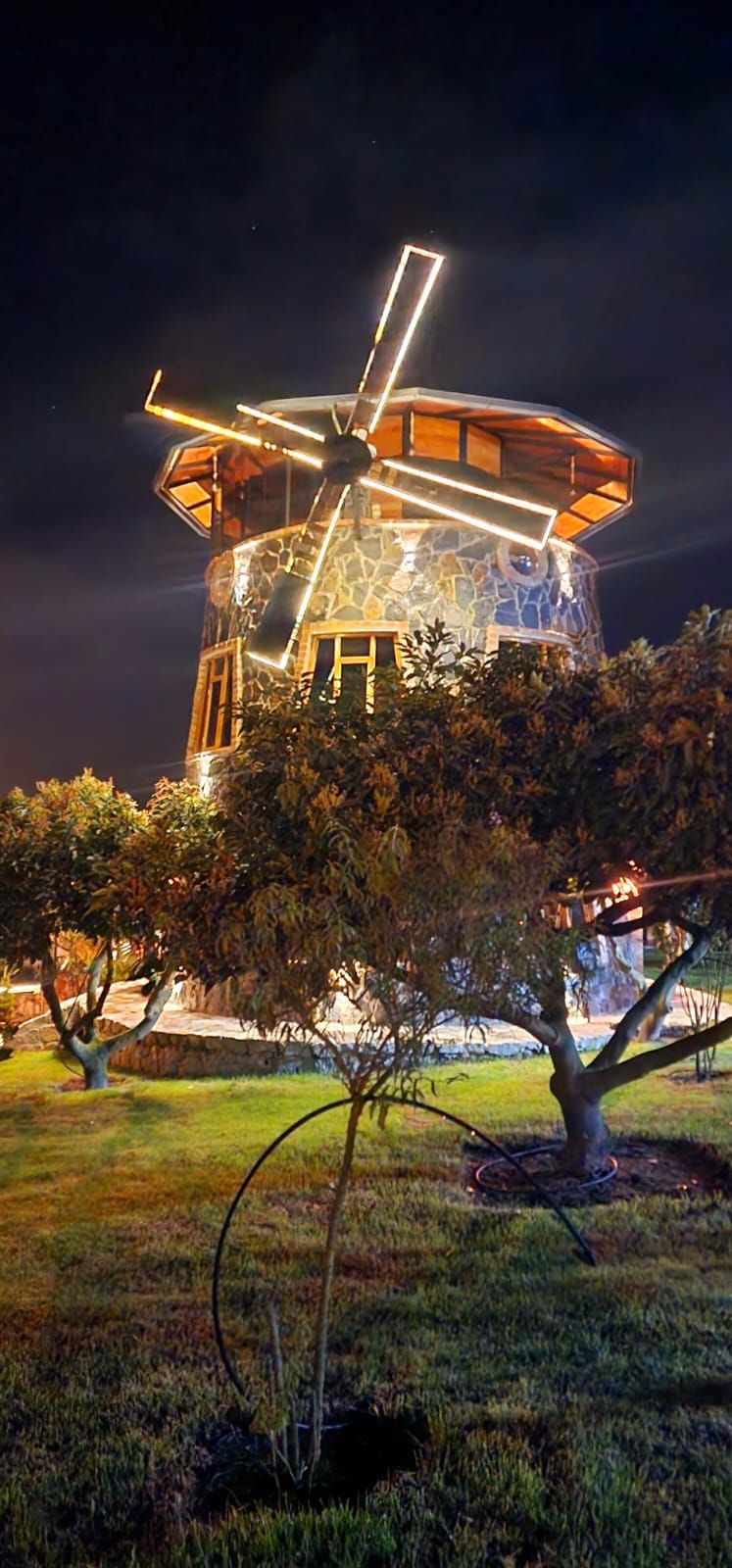 Un molino de viento de diseño moderno, rodeado por un jardín cuidado con árboles y césped.