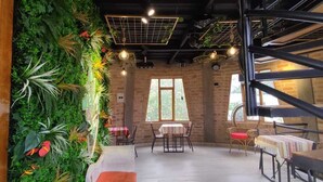 A restaurant with a rustic brick wall, green plants, and a mix of wooden and metal furniture.