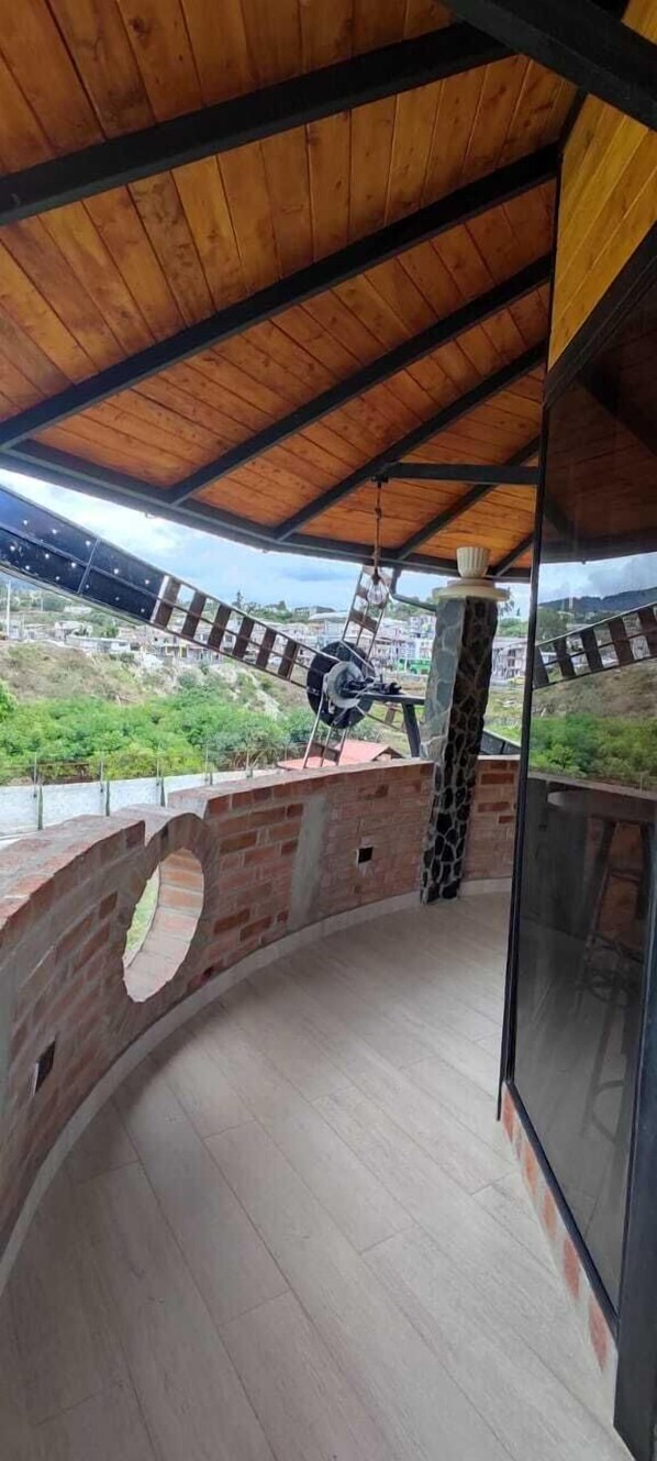 A covered balcony with a curved brick wall, a wooden ceiling, and a view of a green landscape. - Hostería Molino de Café (Santa Rosa de Cusubamba)