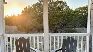 A wooden deck with two Adirondack chairs facing a scenic view of trees and a sunset.