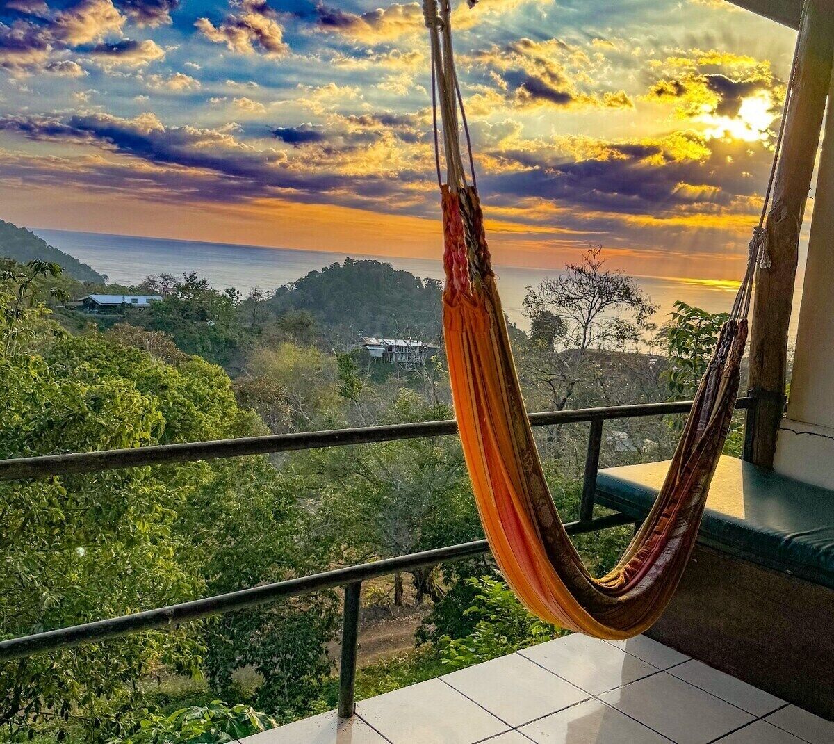Una hamaca colgada en un balcón con vistas a un paisaje montañoso y al océano.