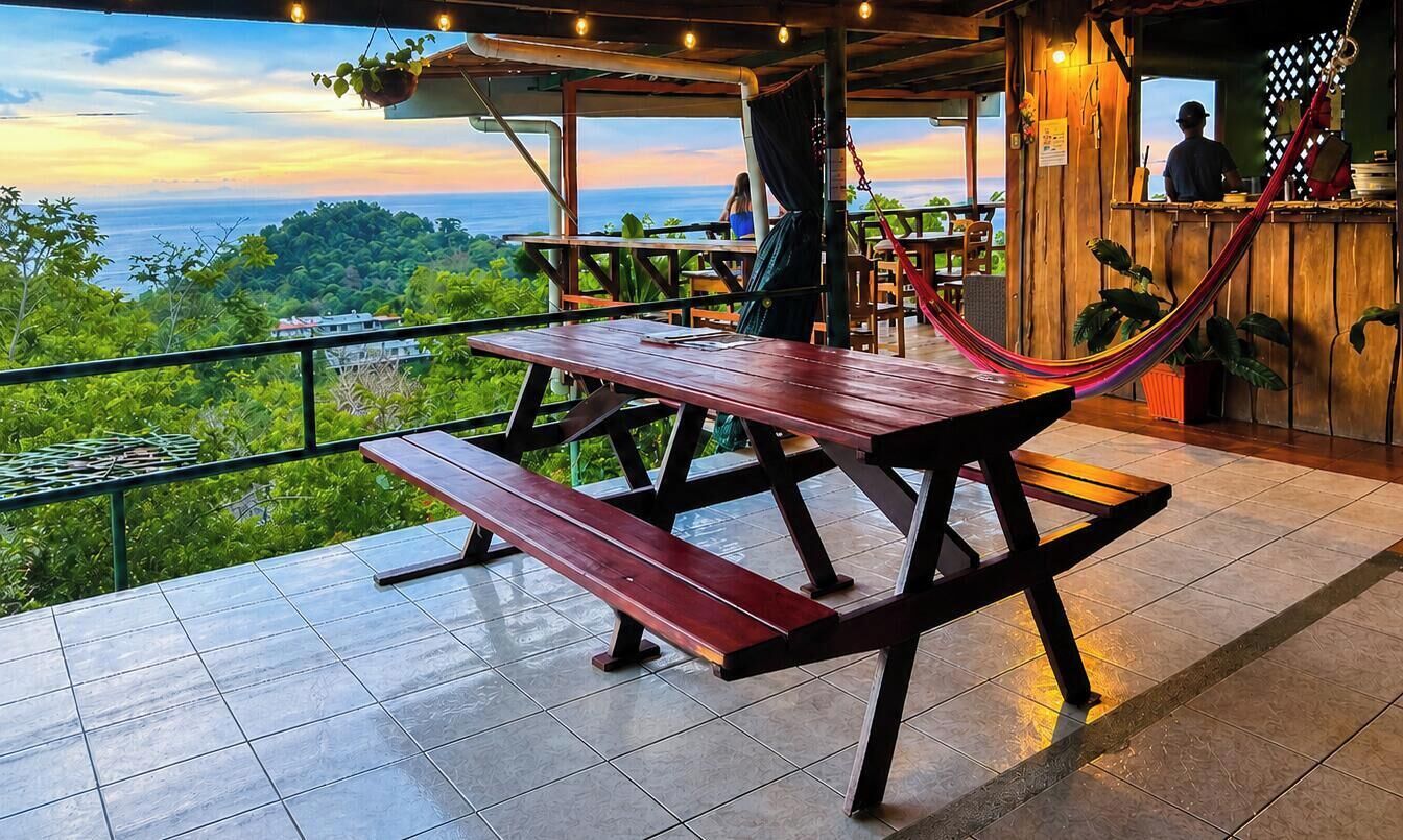 Eine Holzterrasse mit Picknicktischen und einer Hängematte mit Blick auf eine üppige Landschaft.