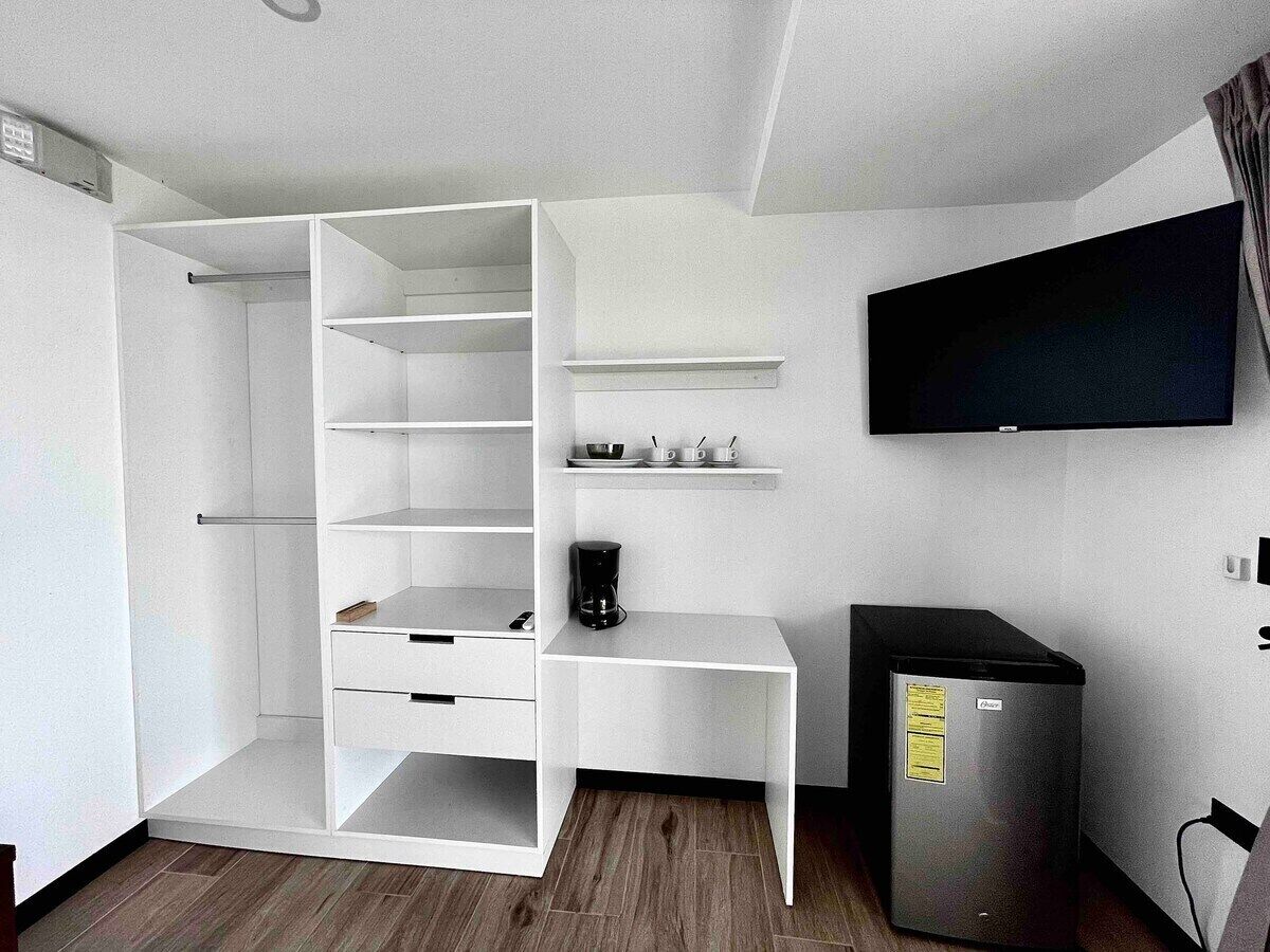 A compact room with a built-in wardrobe, a flat-screen TV mounted on the wall, and a small refrigerator.