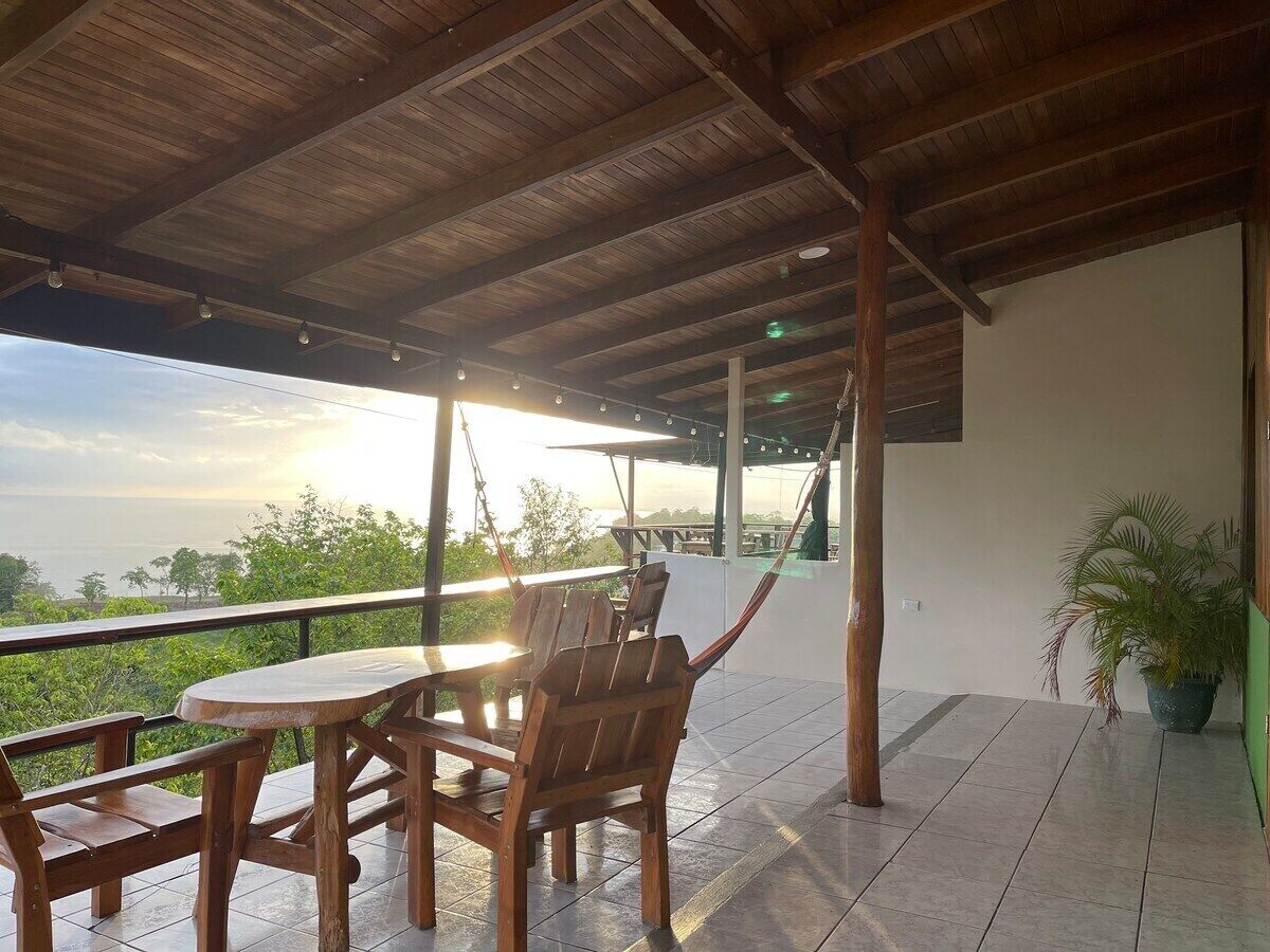 A covered outdoor seating area with wooden furniture and a view of the sea.