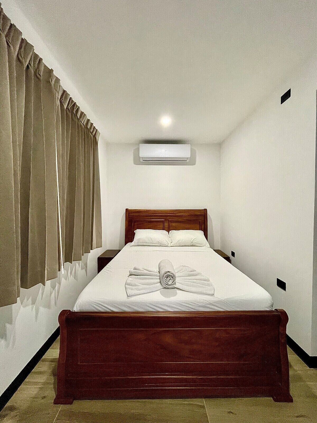 A neatly made bed with a wooden headboard, a rolled towel, and a white pillow.