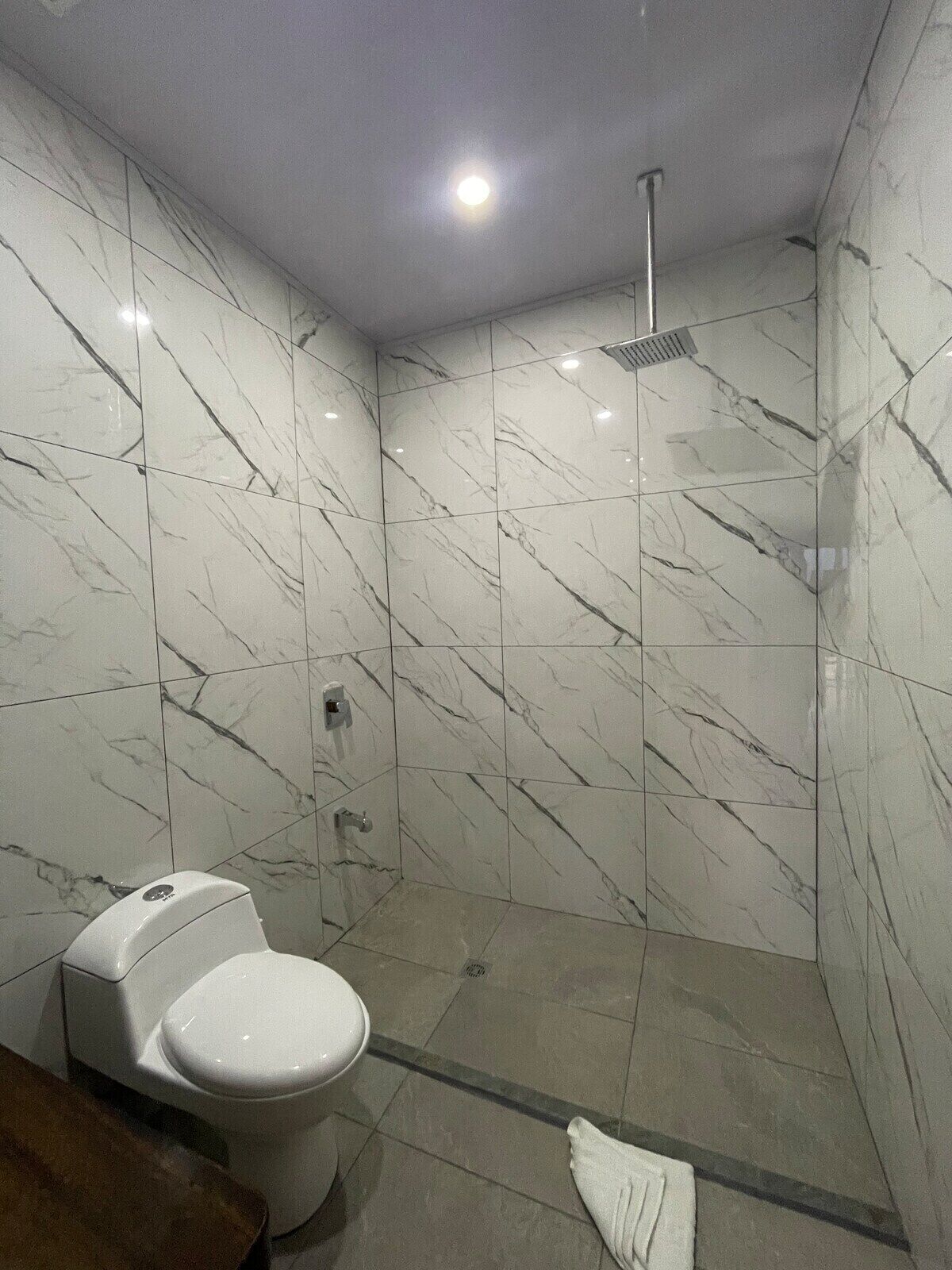A bathroom with a toilet, a shower, and marble walls.