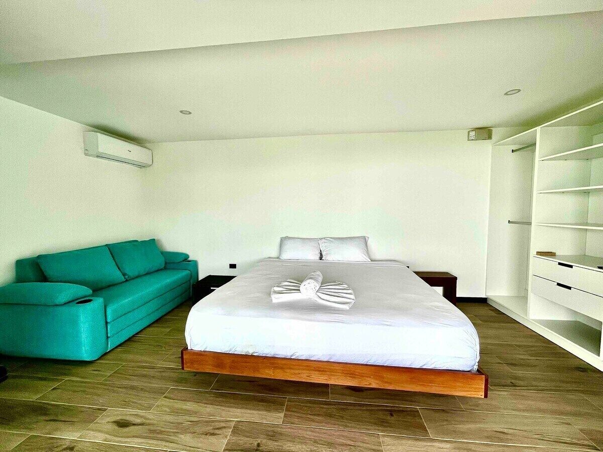 Une chambre d’hôtel moderne avec un grand lit, un canapé de couleur turquoise et une bibliothèque intégrée.