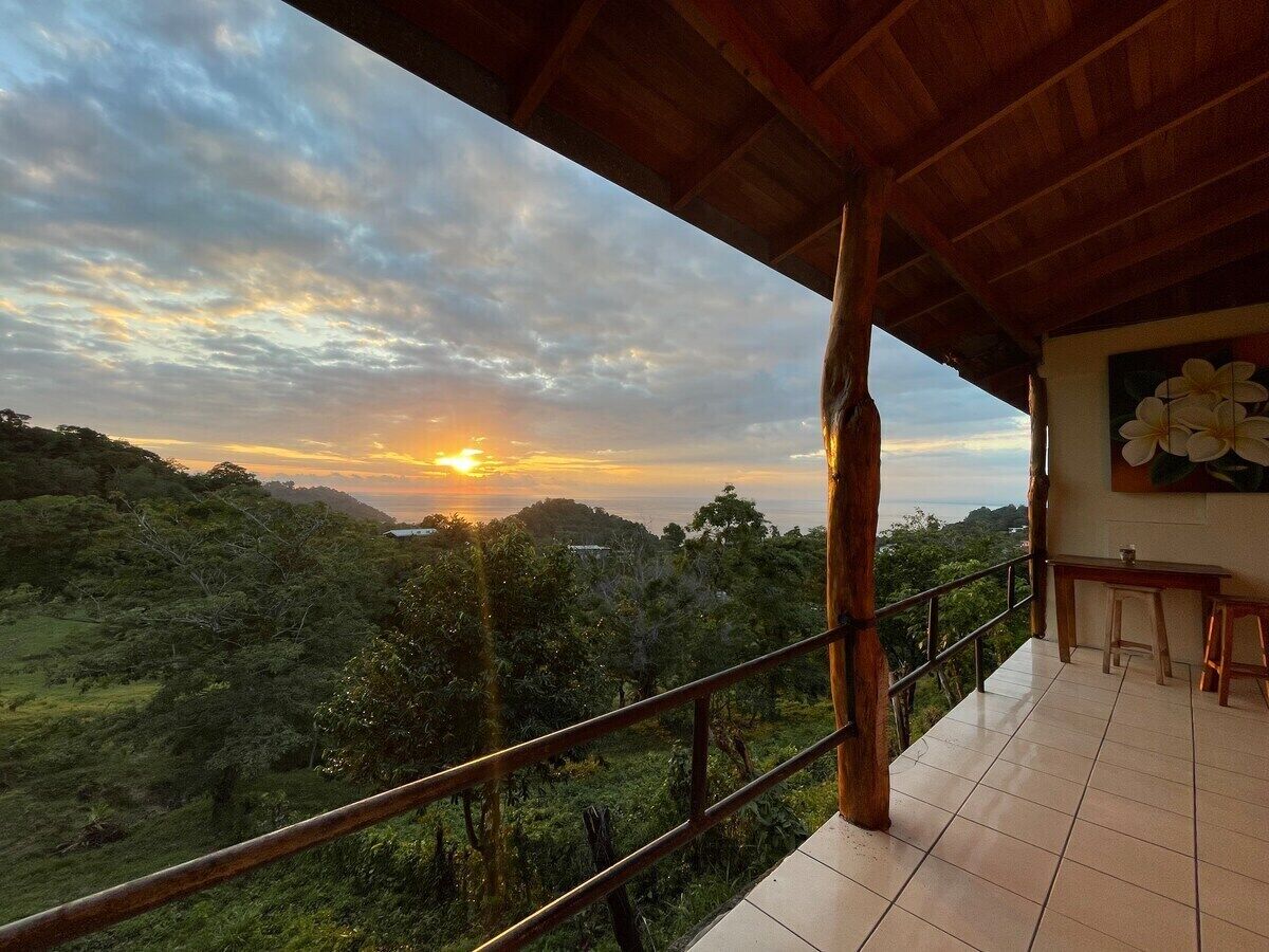 A balcony with a view of a sunset over a lush landscape.