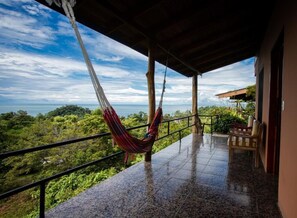 A covered outdoor area with a hammock, a chair, and a view of the ocean. - Pura Natura Lodge (Quepos)