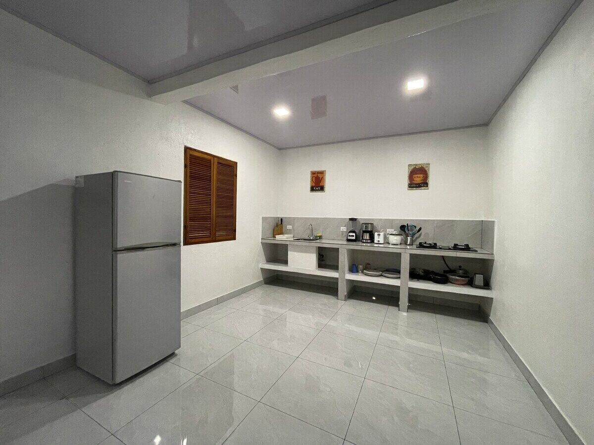 A compact kitchen with a built-in refrigerator, a countertop with a coffee maker, and a shelf with kitchenware.