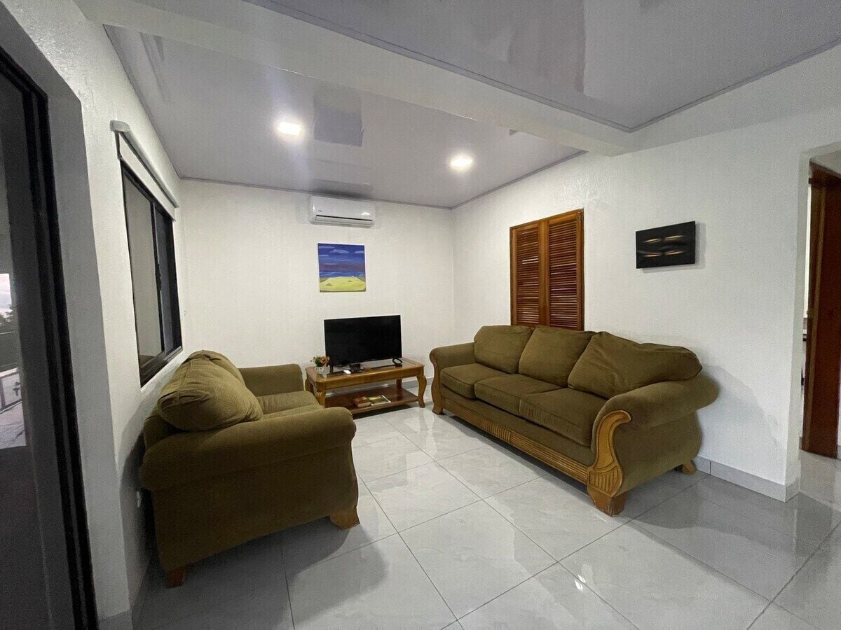 Sala de estar com sofá, televisão sobre um suporte e um quadro na parede.