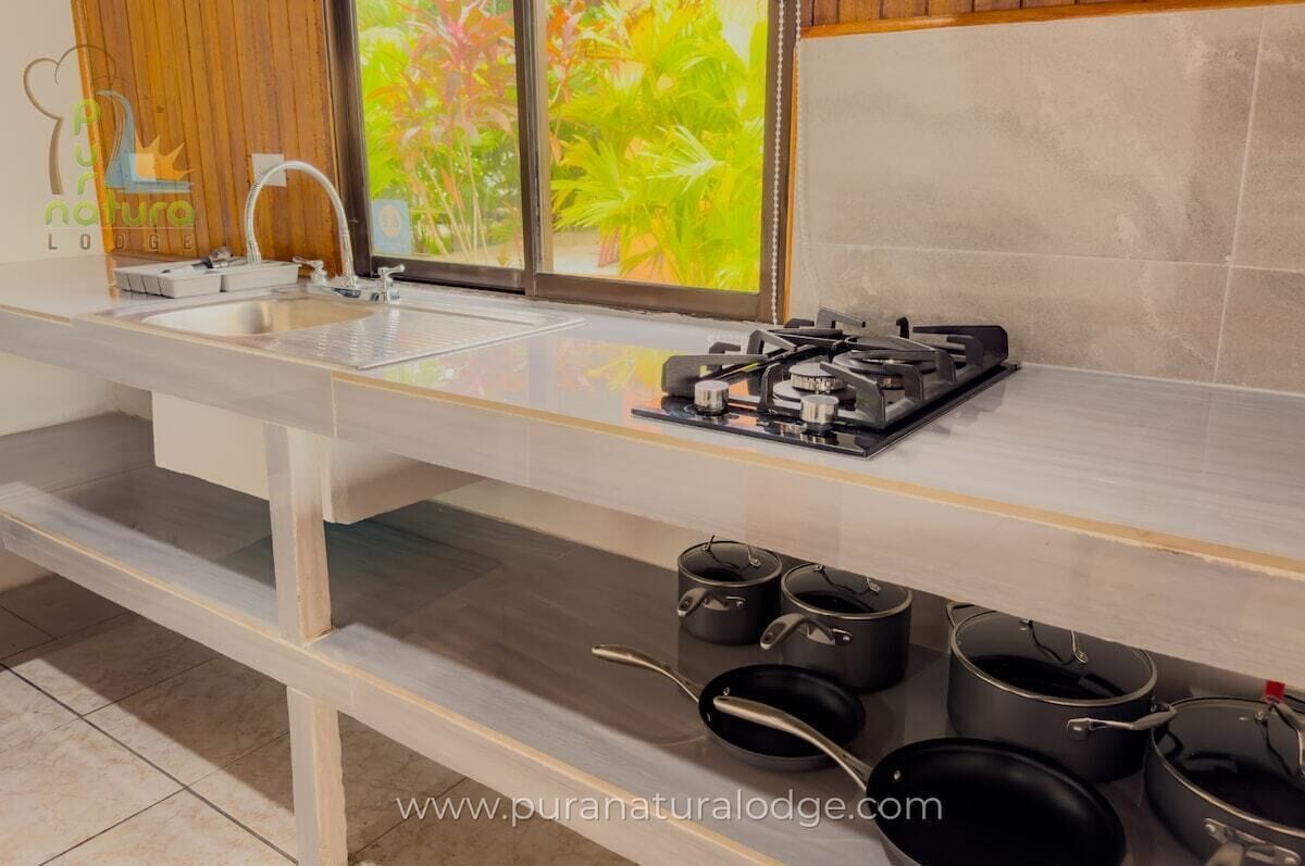 A kitchen with a modern design, featuring a stainless steel sink, a gas stove, and several pots and pans stored below the counter.