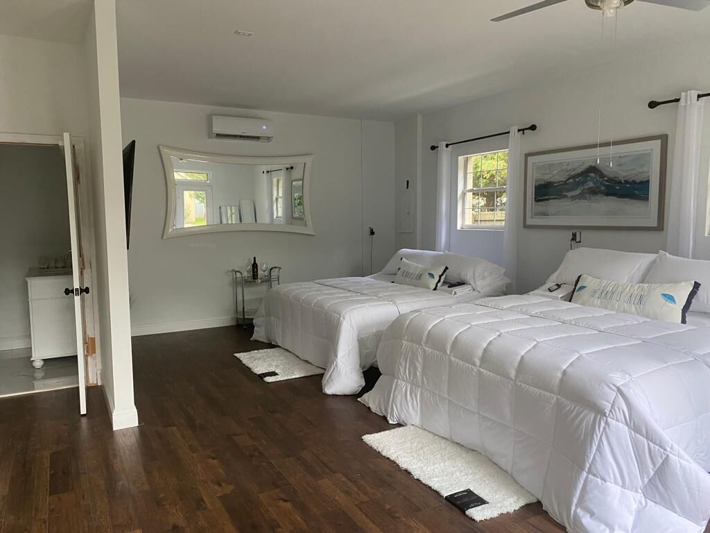A bedroom with two beds, a large mirror, a painting, and a white door.