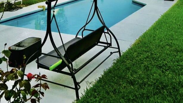 Une piscine avec un fauteuil suspendu, des palmiers et une terrasse en bois.
