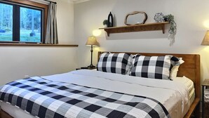 A neatly made bed with a checkered bedspread, a bedside lamp, and a shelf with decorative items.