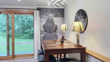 A dining area with a wooden table, two chairs, a lamp, and a bear mural on the wall.