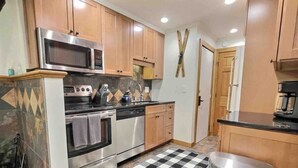 A compact kitchen with wooden cabinets, stainless steel appliances, and a checkered floor mat.