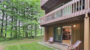 A two-story building with a balcony, a grassy yard, and two lounge chairs.
