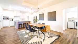 A modern kitchen with white cabinets, a central island, and a dining area with a table and chairs. - Chic New Build - 5 miles to Tech/Covenant/UHC - 2 miles to shopping! (Lubbock)