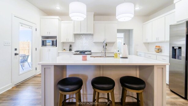 A modern kitchen with white cabinetry, a central island with stools, and stainless steel appliances. - Chic New Build - 5 miles to Tech/Covenant/UHC - 2 miles to shopping! (Lubbock)