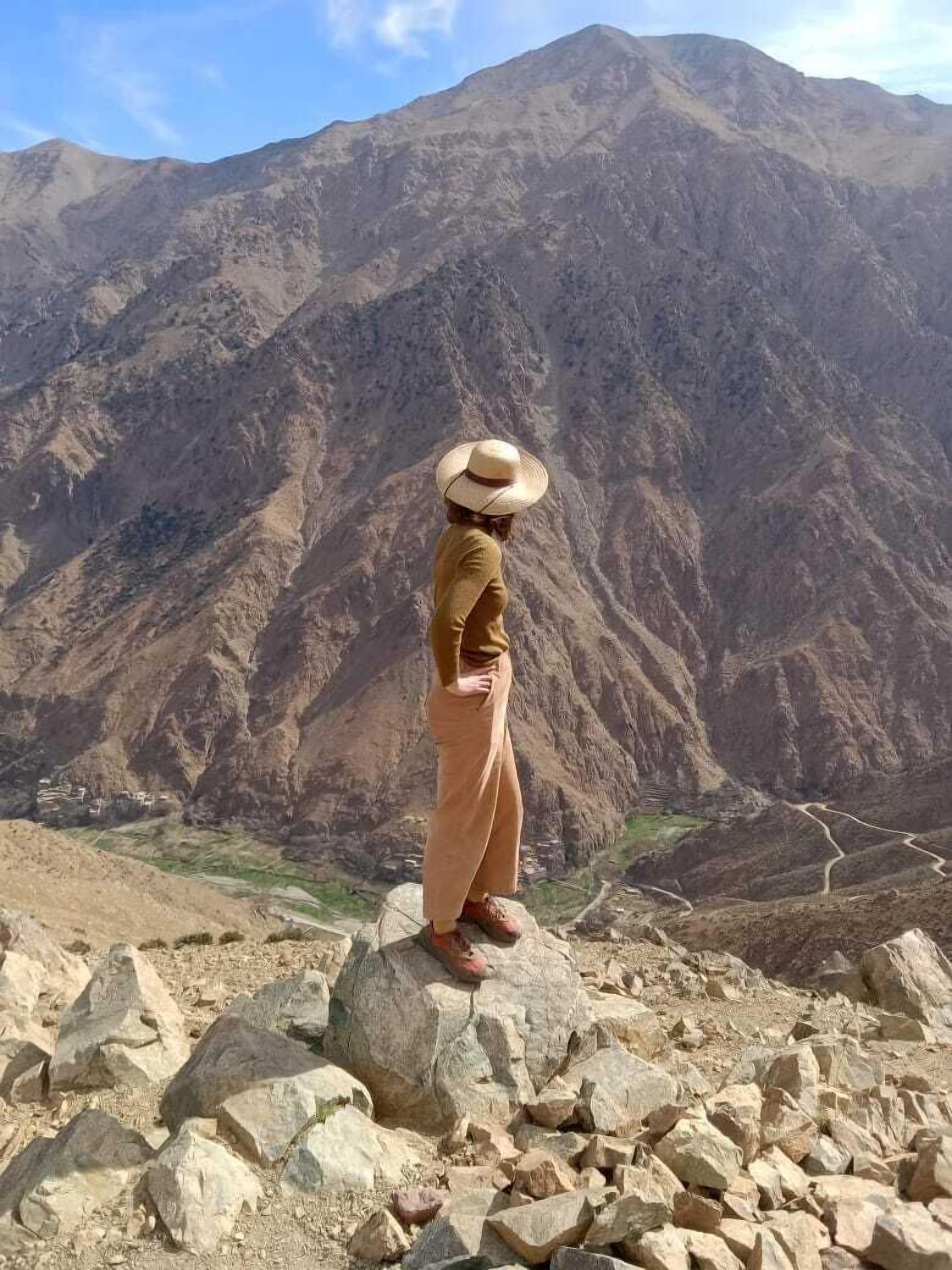 A person standing on a rocky outcrop with a mountainous landscape in the background.