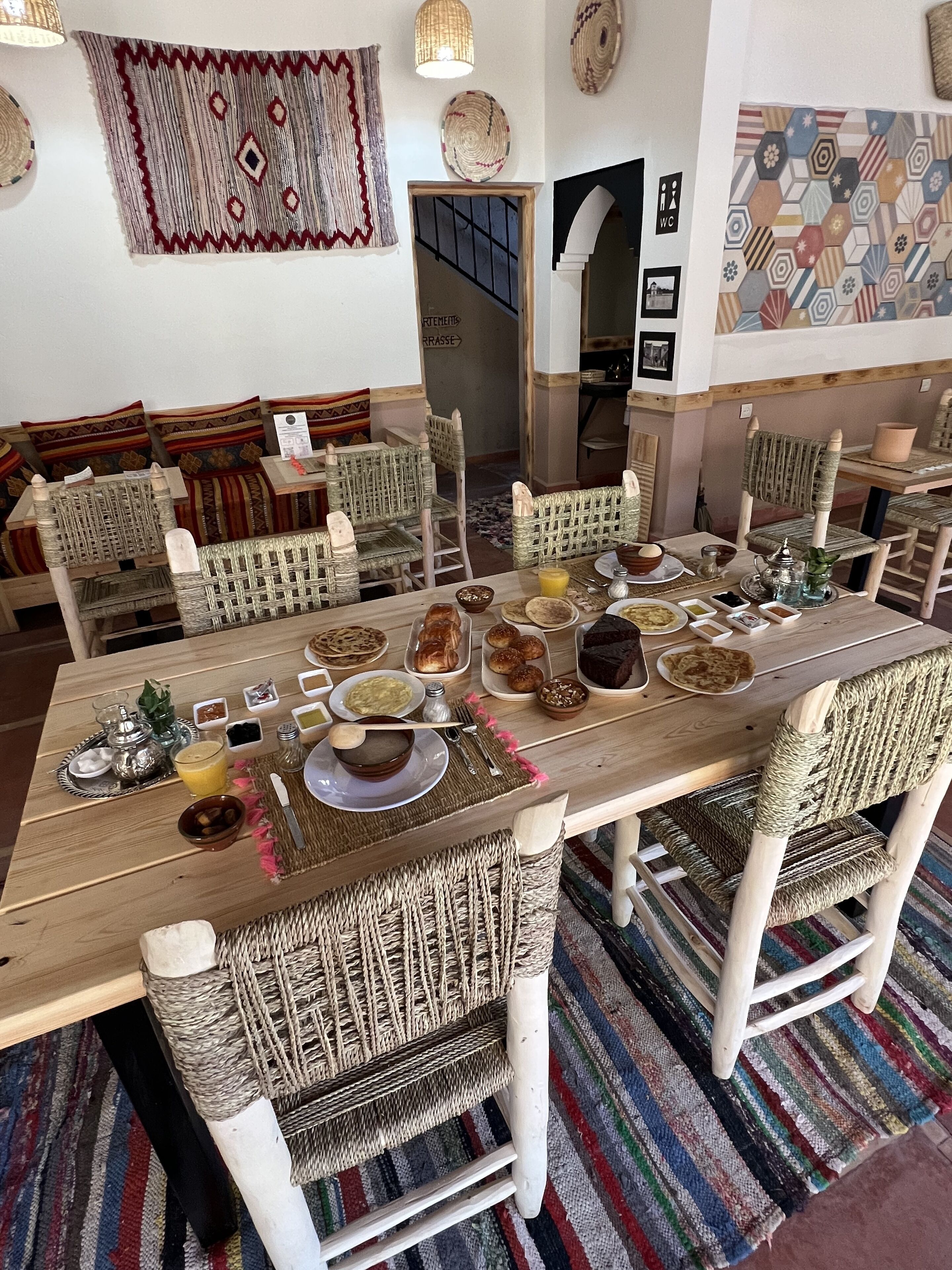 Un comedor con una larga mesa de madera dispuesta para una comida, rodeado de sillas de mimbre.