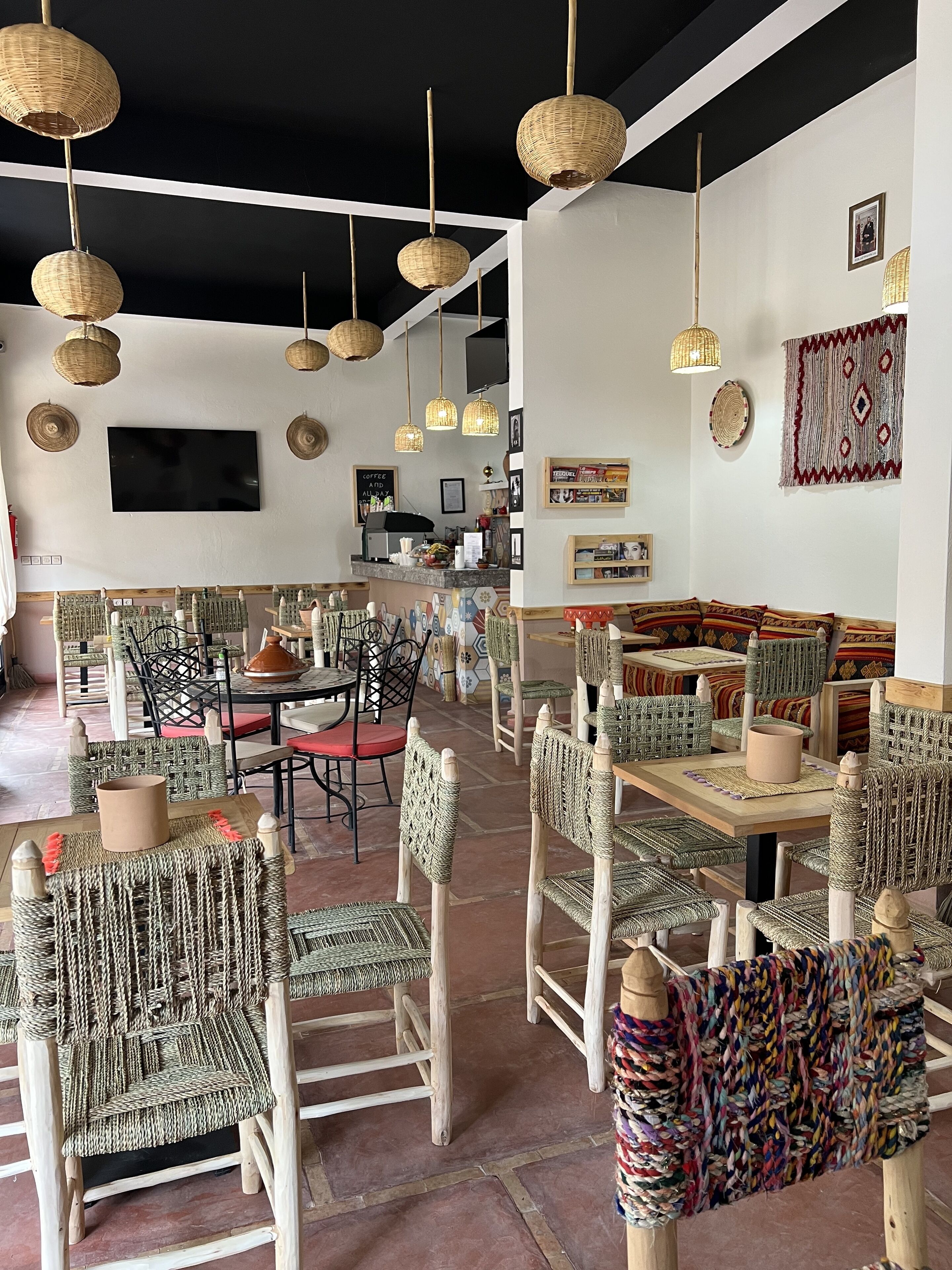 Un restaurant avec des meubles en osier, des lampes en osier suspendues au plafond et un téléviseur fixé au mur.