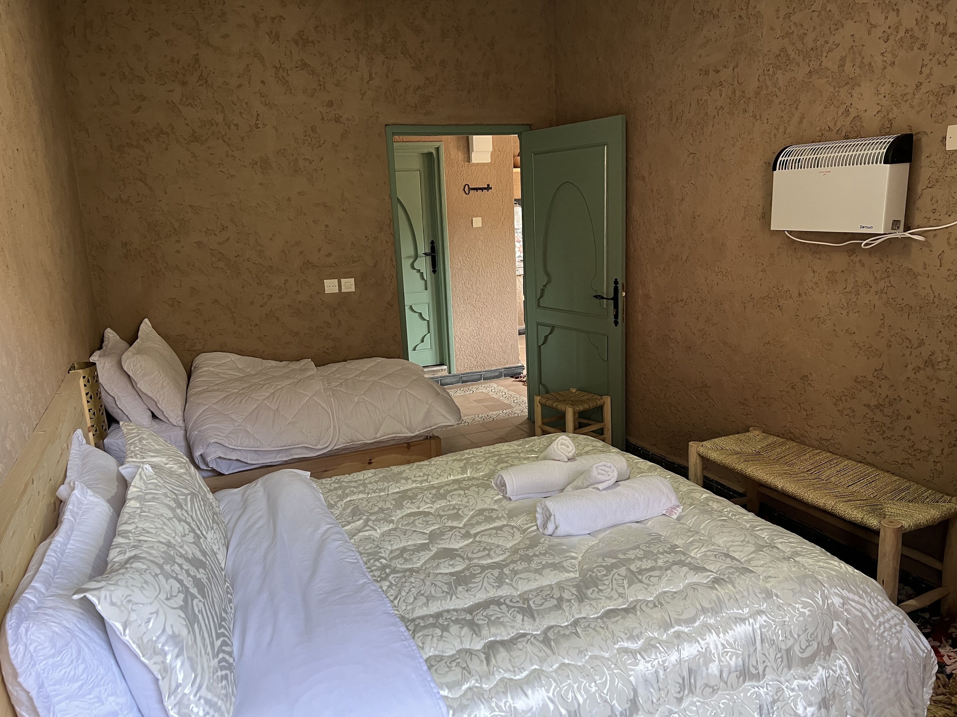A bedroom with two beds, a small wooden stool, and an air conditioning unit on the wall.