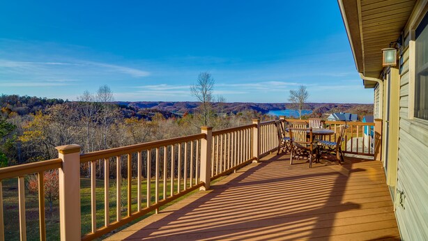 Eine Holzterrasse mit Geländer, Tisch und Stühlen mit Blick auf eine malerische Landschaft aus Bäumen und einem Gewässer.