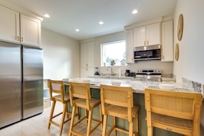 Una cocina moderna con armarios blancos, electrodomésticos de acero inoxidable y una isla central con taburetes de bar.