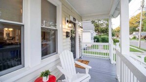Une véranda blanche avec une table rouge et deux chaises Adirondack blanches.