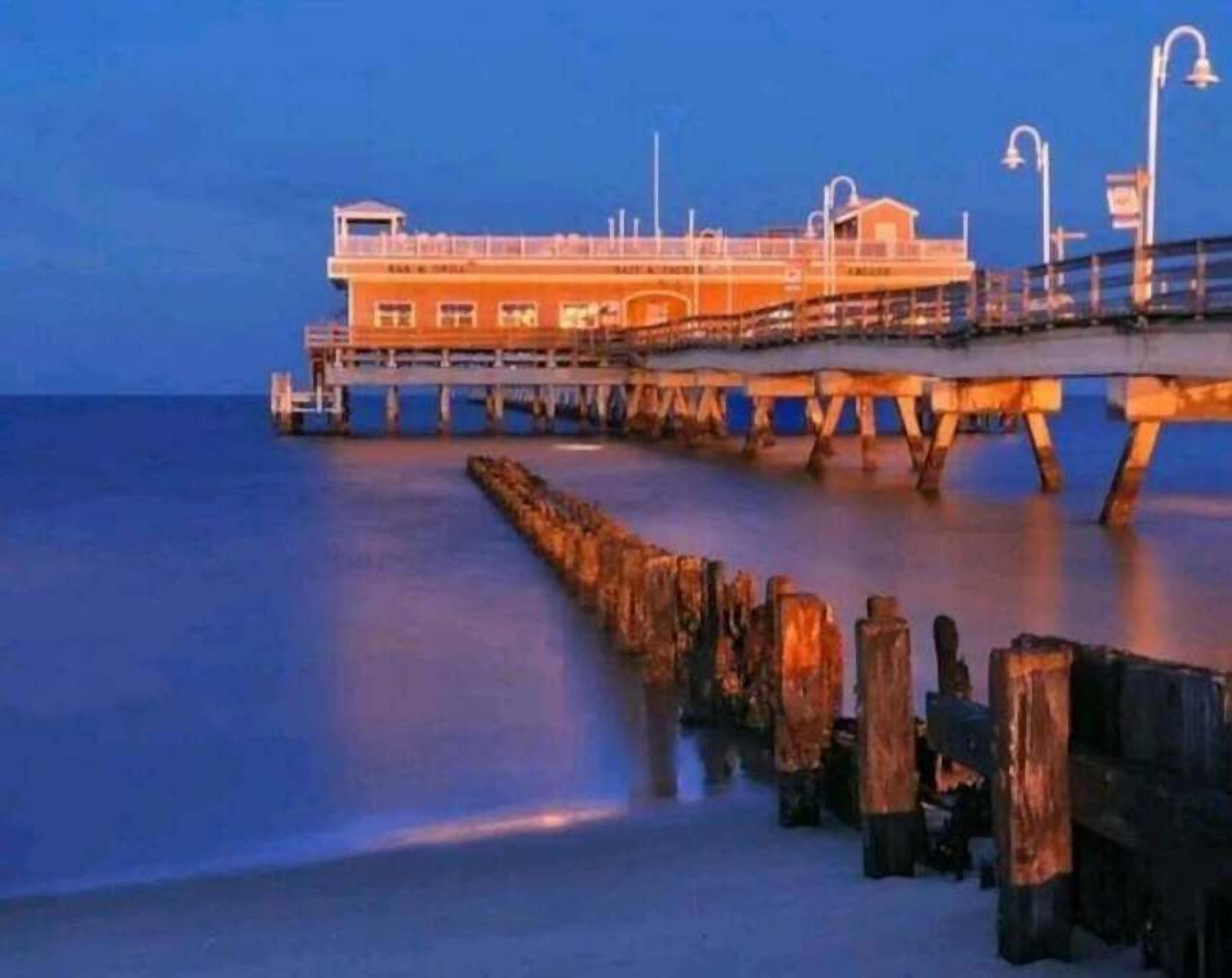 Un muelle que se adentra en el agua con un edificio, que cuenta con techo plano y varias ventanas.