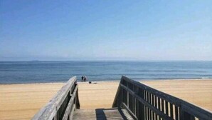 Une promenade en bois qui mène à une plage, sous un ciel dégagé.